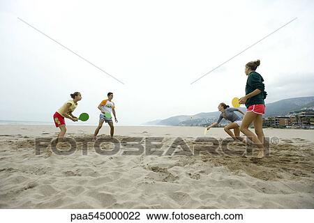 Stock Image - Teen friends playing paddleball on beach. Fotosearch