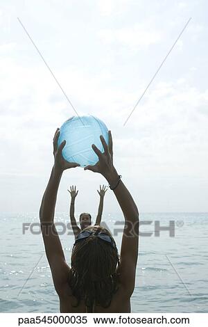 Stock Photography - Teen girls playing with beach ball in sea. Fotosearch