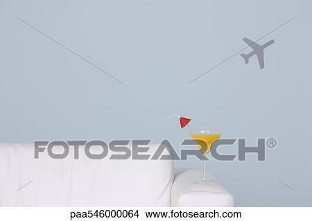 Cocktail on arm of sofa, airplane shape in background View Large Photo Image Picture - Cocktail on arm of sofa, airplane shape in background. Fotosearch