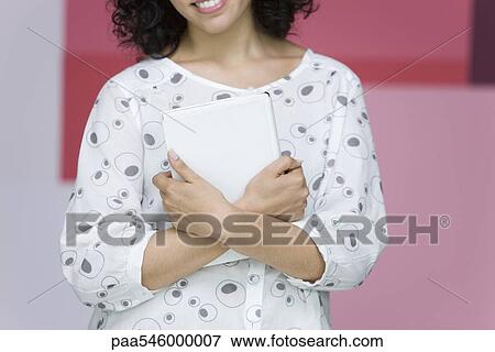 Woman holding book to chest, smiling, cropped View Large Photo Image Stock Photo - Woman holding book to chest, smiling, cropped. Fotosearch