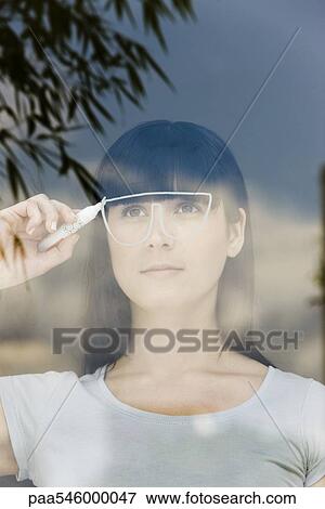 Stock Photo - Young woman drawing a pair of glasses on a window pane, looking through window. Fotosearch