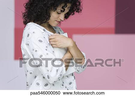 Young woman holding book tightly against chest, smiling View Large Photo Image Stock Image - Young woman holding book tightly against chest, smiling. Fotosearch
