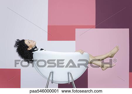Stock Image - Young woman reclining in armchair. Fotosearch