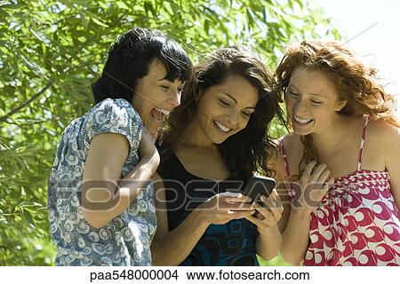 "Three young women outdoors, looking at smartphone together" View Large Photo Image Picture - "Three young women outdoors, looking at smartphone together". Fotosearch