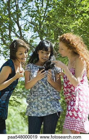 "Three young women standing outdoors, looking at smartphone" View Large Photo Image Stock Photo - "Three young women standing outdoors, looking at smartphone". Fotosearch