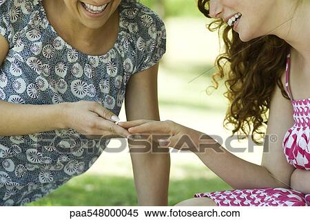"Two women sitting outdoors, looking at one woman's hand, both smiling" View Large Photo Image Stock Photography - "Two women sitting outdoors, looking at one woman's hand, both smiling". Fotosearch