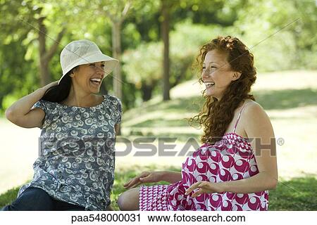"Two young women chatting outdoors, both smiling" View Large Photo Image Stock Image - "Two young women chatting outdoors, both smiling". Fotosearch