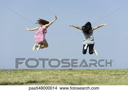 "Two young women jumping in midair outdoors, rear view" View Large Photo Image Picture - "Two young women jumping in midair outdoors, rear view". Fotosearch