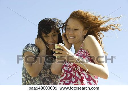 "Two young women outdoors, listening to MP3 player together" View Large Photo Image Stock Photography - "Two young women outdoors, listening to MP3 player together". Fotosearch