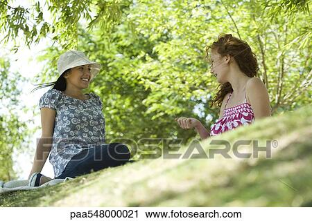 "Two young women sitting in park talking, low angle view" View Large Photo Image Stock Image - "Two young women sitting in park talking, low angle view". Fotosearch