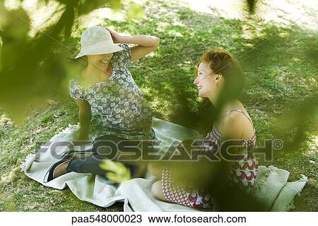 "Two young women sitting on blanket, talking, viewed through foliage" View Large Photo Image Stock Image - "Two young women sitting on blanket, talking, viewed through foliage". Fotosearch