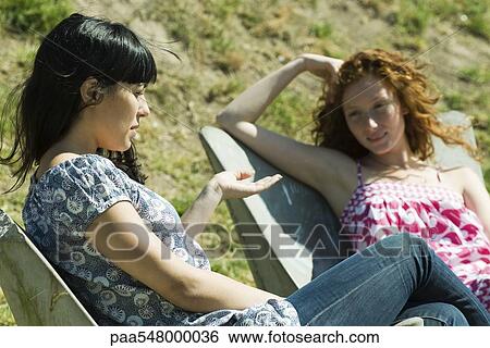 "Two young women sitting outdoors, talking" View Large Photo Image Stock Photograph - "Two young women sitting outdoors, talking". Fotosearch