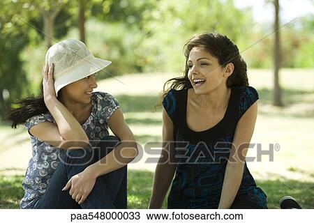 "Two young women talking outdoors, one holding sun hat on head" View Large Photo Image Stock Image - "Two young women talking outdoors, one holding sun hat on head". Fotosearch