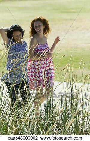 "Two young women walking arm in arm outdoors, both laughing" View Large Photo Image Stock Image - "Two young women walking arm in arm outdoors, both laughing". Fotosearch