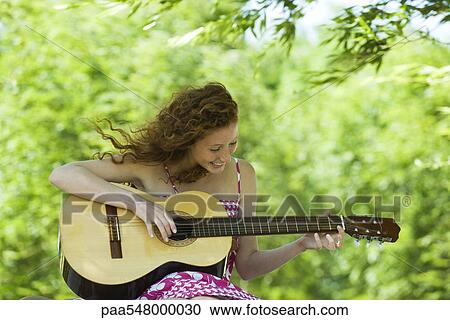 Young woman playing acoustic guitar outdoors View Large Photo Image Stock Image - Young woman playing acoustic guitar outdoors. Fotosearch