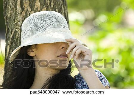 Stock Photo - Young woman pulling sun hat over eyes. Fotosearch
