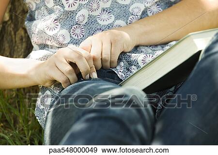 "Young woman sitting on ground with book on lap, reaching for something in pocket" View Large Photo Image Stock Photo - "Young woman sitting on ground with book on lap, reaching for something in pocket". Fotosearch
