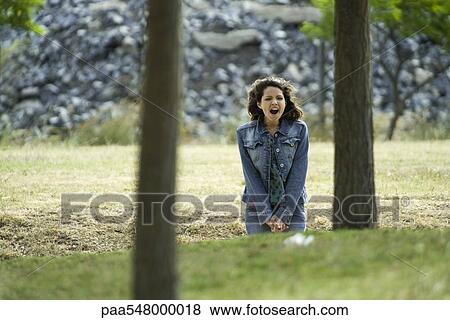 Stock Photo - Young woman sitting outdoors with mouth wide open. Fotosearch