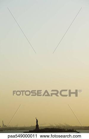 Stock Image - Statue of Liberty beneath evening sky discolored by smog. Fotosearch