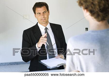 Stock Photography - Businessman holding clipboard speaking to associate. Fotosearch