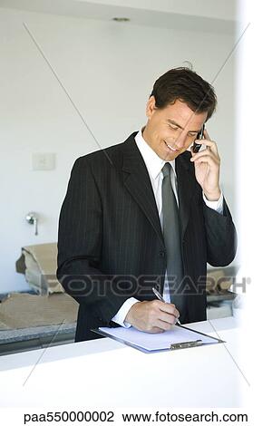 Stock Image - "Businessman phoning, writing notes on clipboard pad". Fotosearch