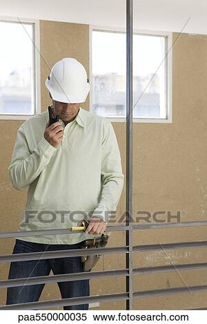 Stock Photography - Construction supervisor at interior railing using walkie-talkie looking down. Fotosearch