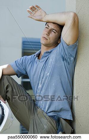 Stock Image - "Construction worker holding back of arm to forehead, eyes closed, taking break". Fotosearch