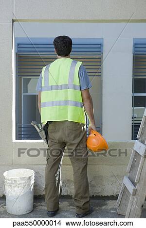 Picture - Construction worker holding hard hat looking out window. Fotosearch