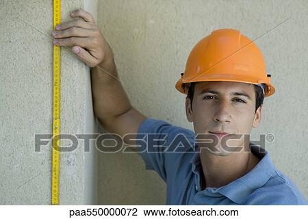 "Construction worker holding ruler against wall, looking at camera" View Large Photo Image Stock Image - "Construction worker holding ruler against wall, looking at camera". Fotosearch