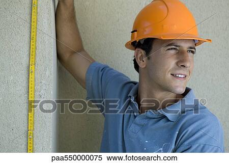Stock Photography - "Construction worker holding ruler against wall, looking away". Fotosearch