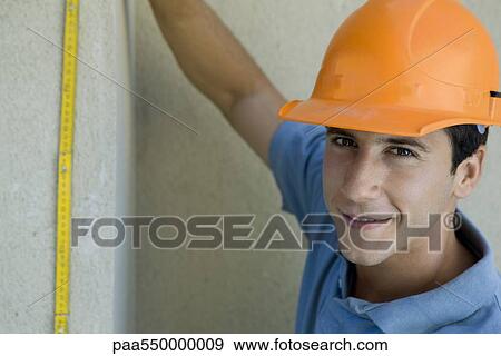Stock Photo - Construction worker holding ruler up against wall. Fotosearch