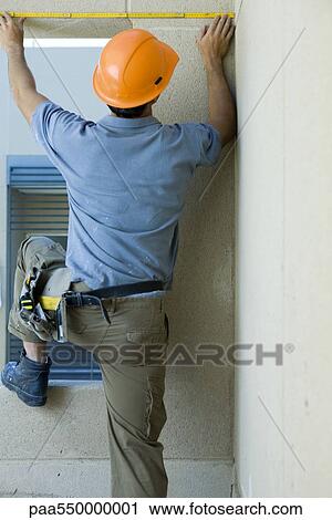 Stock Image - Construction worker measuring space above window. Fotosearch