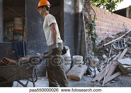 Stock Photograph - Construction worker moving wheelbarrow through construction site. Fotosearch