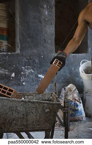 Stock Image - Construction worker placing brick in wheelbarrow. Fotosearch