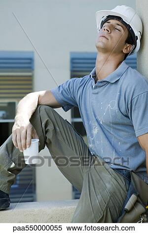Stock Photography - "Construction worker sitting on ledge, leaning head back, eyes closed, taking break". Fotosearch