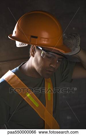Stock Photograph - Construction worker taking hard hat off wiping brow with back of hand. Fotosearch