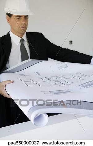 Stock Photo - Man in suit and hard hat unrolling blueprint. Fotosearch