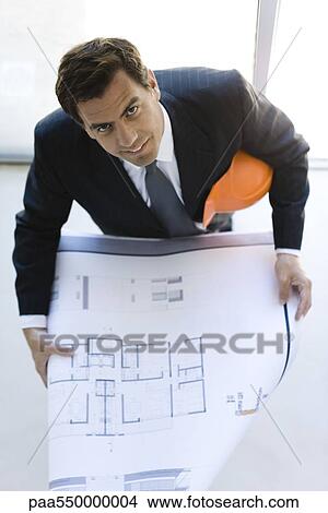 Picture - Man in suit holding blueprints looking up at camera. Fotosearch