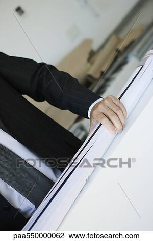 Stock Image - Man in suit holding rolled up blueprint. Fotosearch