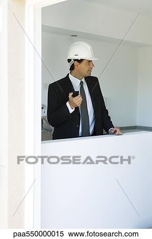 Man in suit wearing hard hat holding walkie-talkie looking out window View Large Photo Image Stock Photography - Man in suit wearing hard hat holding walkie-talkie looking out window. Fotosearch