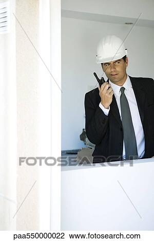 "Man in suit, wearing hard hat, using walkie talkie, looking out window" View Large Photo Image Stock Image - "Man in suit, wearing hard hat, using walkie talkie, looking out window". Fotosearch