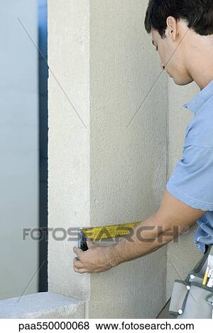 Stock Photo - Man measuring space along wall. Fotosearch