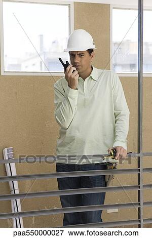 Stock Photo - Man standing at interior railing using walkie talkie. Fotosearch