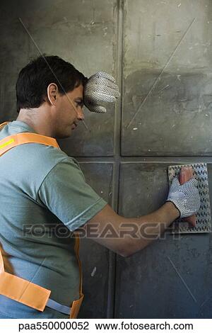 Stock Image - "Mason with trowel pausing work, back of hand held to forehead". Fotosearch