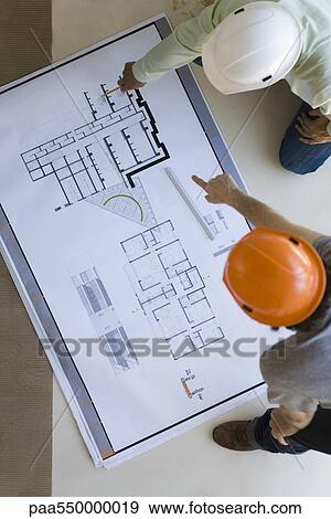 Two men crouching discussing blueprints spread out on floor View Large Photo Image Stock Photo - Two men crouching discussing blueprints spread out on floor. Fotosearch