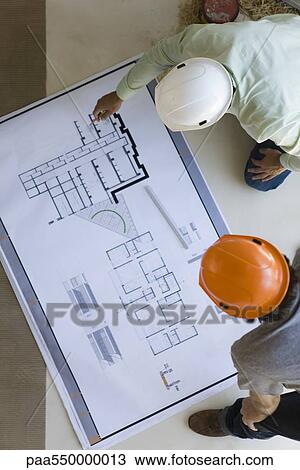 Two men crouching looking over blueprints spread out on floor View Large Photo Image Stock Image - Two men crouching looking over blueprints spread out on floor. Fotosearch