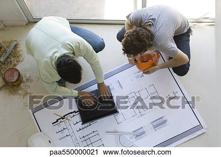 "Two men crouching using laptop, looking at blueprint spread out on floor" View Large Photo Image Stock Image - "Two men crouching using laptop, looking at blueprint spread out on floor". Fotosearch