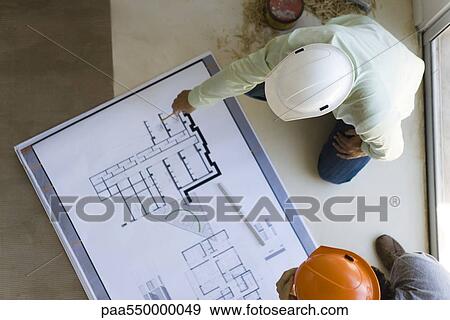 Stock Photo - Two men reviewing blueprint spread out on floor. Fotosearch