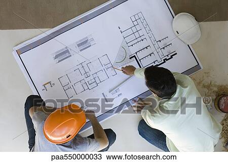 Two men side by side reviewing blueprint spread out on floor View Large Photo Image Stock Image - Two men side by side reviewing blueprint spread out on floor. Fotosearch