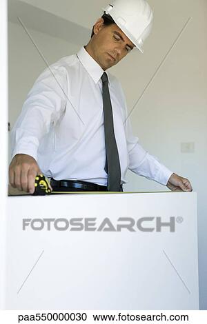 Stock Image - "Well-dressed man measuring ledge, low angle view". Fotosearch